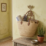 Woven basket with handles on a wooden bench against a light yellow wall.