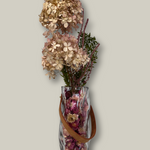 Clear glass vase shaped like a bag with dried flowers on a light gray background