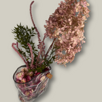 Decorative arrangement of dried flowers in a clear glass vase on a light gray background