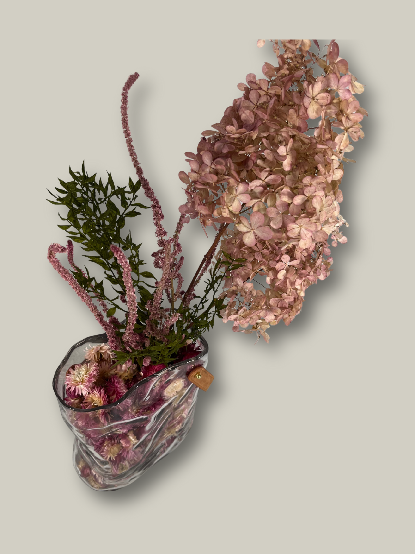 Decorative arrangement of dried flowers in a clear glass vase on a light gray background