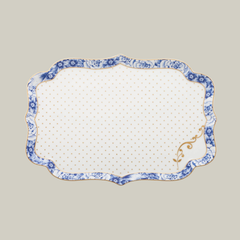 Rectangular porcelain white serving plate with gold and blue floral patterns on a soft green background