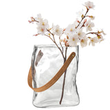 9.5 Inch tall clear glass vase shaped like a paper bag with faux leather holding white flowers. 