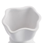 Close-up of the opening of a white ceramic vase with a delicate cinch midway that creates a graceful twist. 
