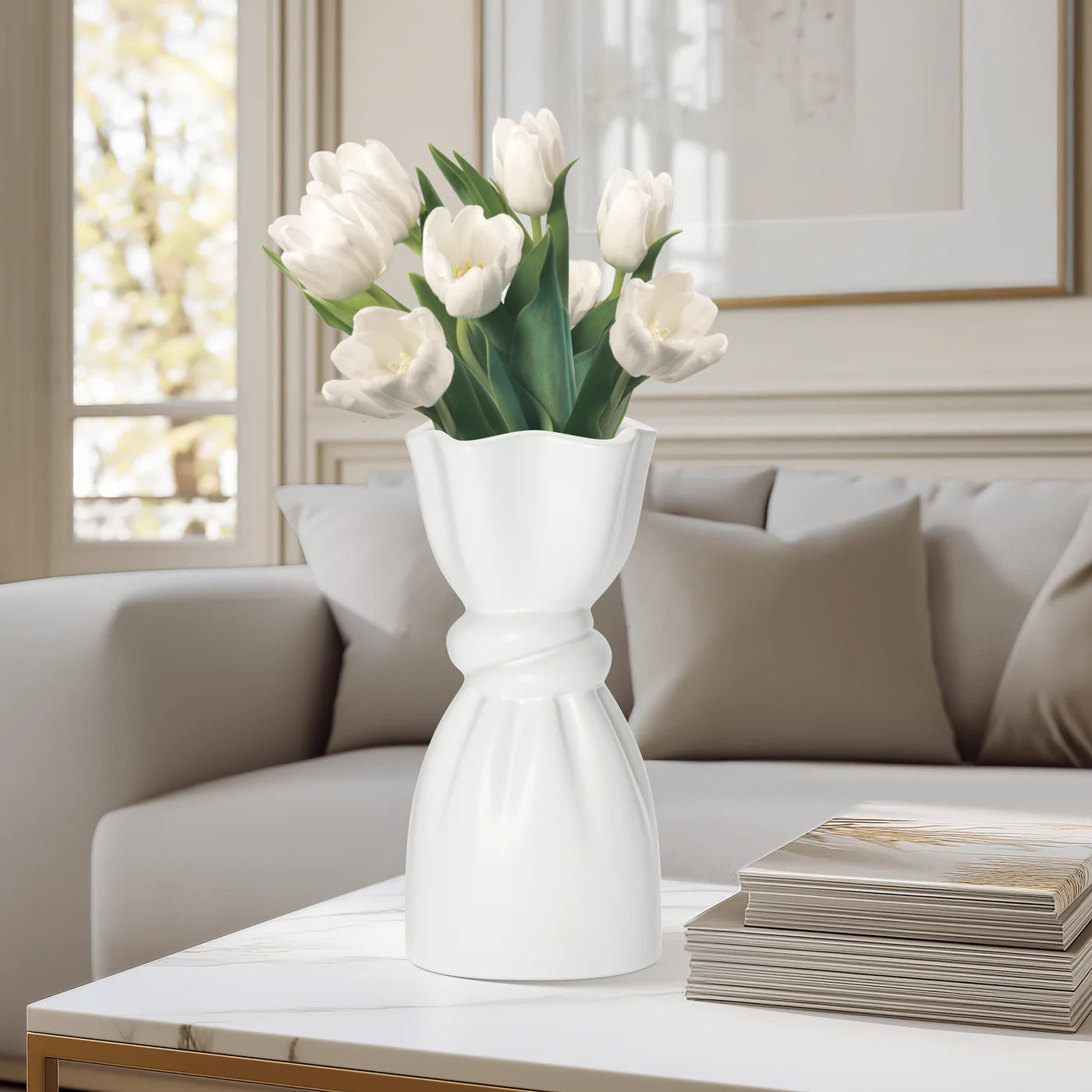 White ceramic vase with a delicate cinch midway that creates a graceful twist holding tulips on a coffee table in a living room setting.