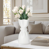 White ceramic vase with a delicate cinch midway that creates a graceful twist holding tulips on a coffee table in a living room setting.