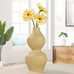Yellow double gourd shaped tall bud vase with ribbed texture holding yellow flowers in a room setting.