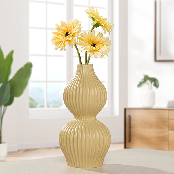 Yellow double gourd shaped tall bud vase with ribbed texture holding yellow flowers in a room setting.