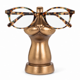 Oval eyeglasses with a tortoiseshell pattern resting on a metallic gold cat-head display stand against a white background.