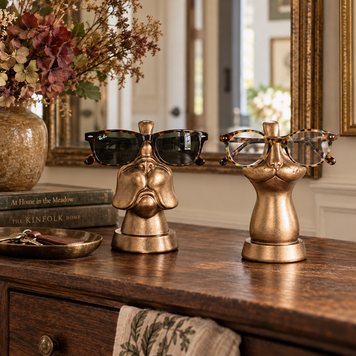 Two decorative metallic gold sunglasses and eyeglasses stands displayed on a wooden console table in a styled interior setting.