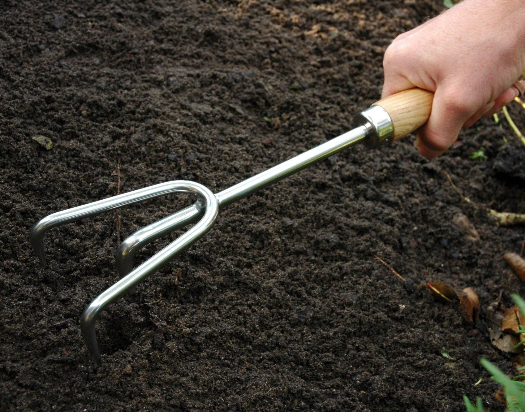 Hand holding a garden fork in dark soil