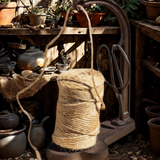 Spool of twine in a iron holder with scissors on a wooden surface with pots and tools in the background