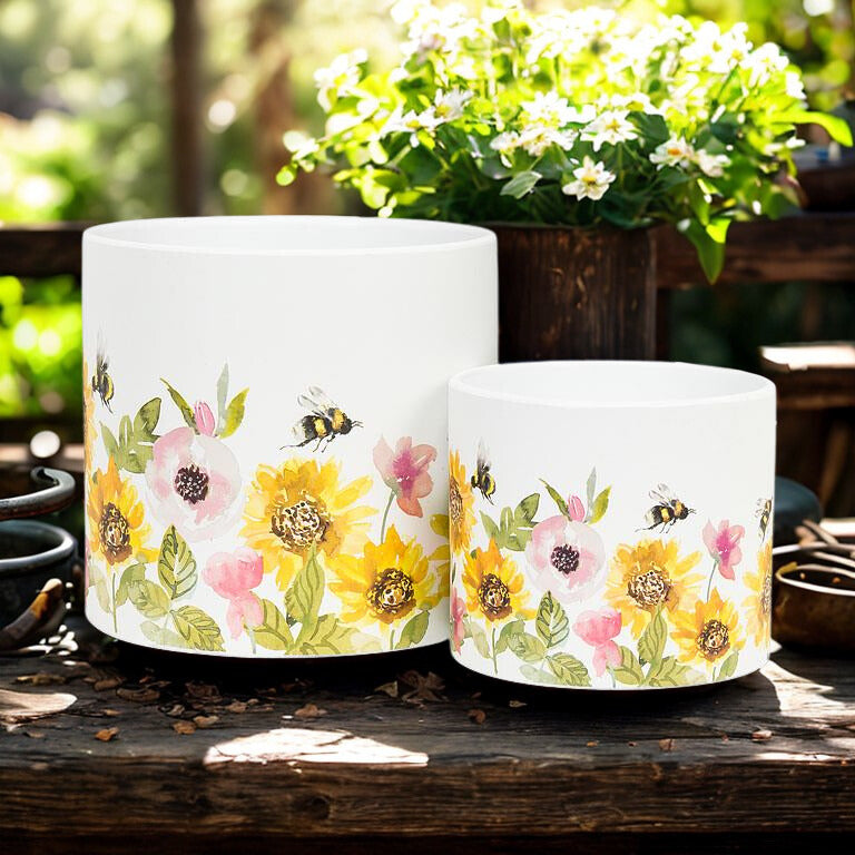 Two white ceramic pots with floral and bee design on a wooden surface.