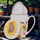White mug with floral design and matching coaster on a wooden surface with plants in the background