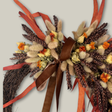 Decorative wreath with dried flowers, ribbons, and a brown bow on a light gray background