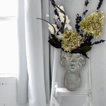 Decorative everlasting flower arrangement in a concrete vase on a white chair against a white curtain background