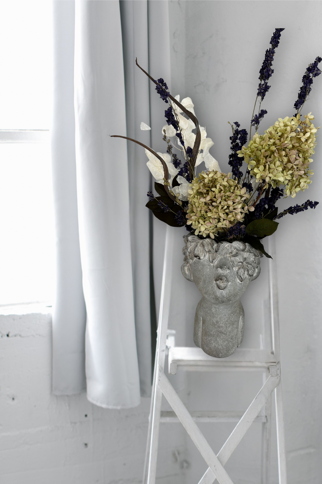 Decorative everlasting flower arrangement in a concrete vase on a white chair against a white curtain background