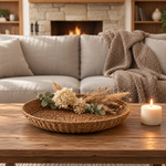Living room scene with a wooden coffee table in the forefront featuring a beautiful seagrass tray with dried flowers.  1
