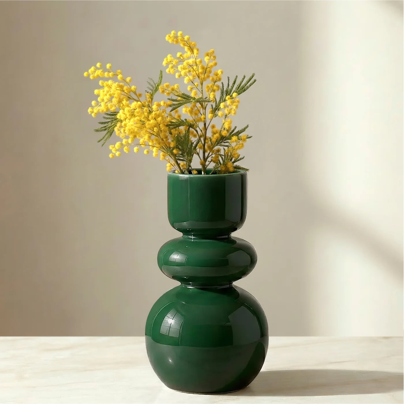Deep glossy green vase with sleek bulb shape holding yellow flowers on a neutral background.