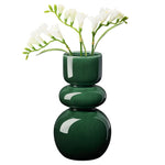 Deep glossy green vase with sleek bulb shape holding white flowers on a white background.