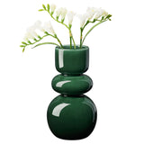 Deep glossy green vase with sleek bulb shape holding white flowers on a white background.