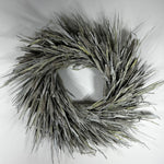 A circular decorative wreath made from dried reeds or cattails in muted gray, beige, and olive tones, photographed against a plain light background.