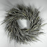 A circular decorative wreath made from dried reeds or cattails in muted gray, beige, and olive tones, photographed against a plain light background.