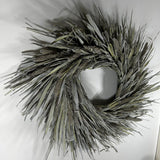 A natural reed wreath made of dried cattails and reeds, featuring textured brown seed heads and long gray-green leaves, displayed against a plain white background.