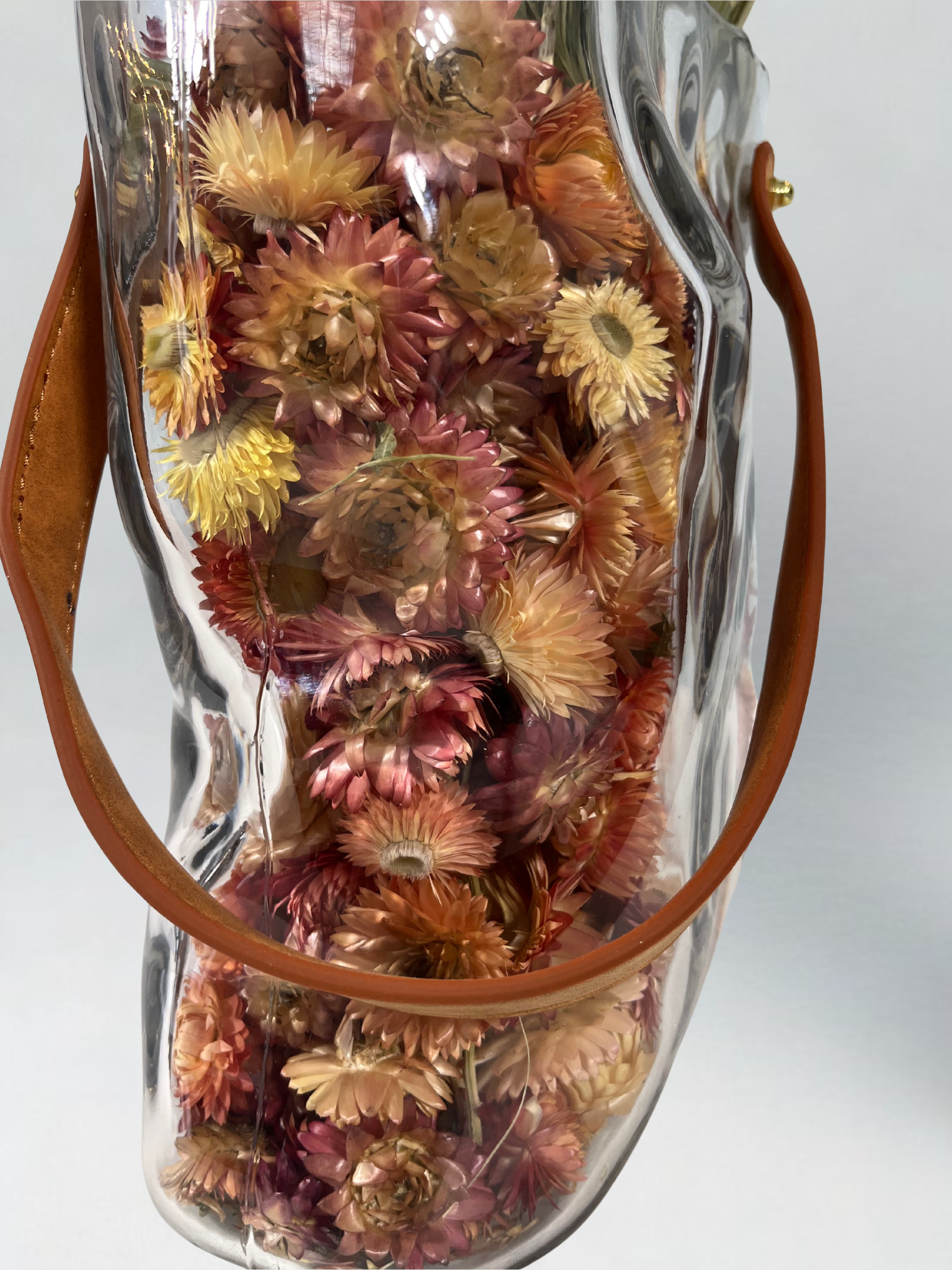 Decorative glass vase shaped like a paper bag with a leather handle filled with dried helichrysum in a natural salmon colour.