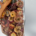 Decorative glass vase shaped like a paper bag with a leather handle filled with dried helichrysum in a natural salmon colour.