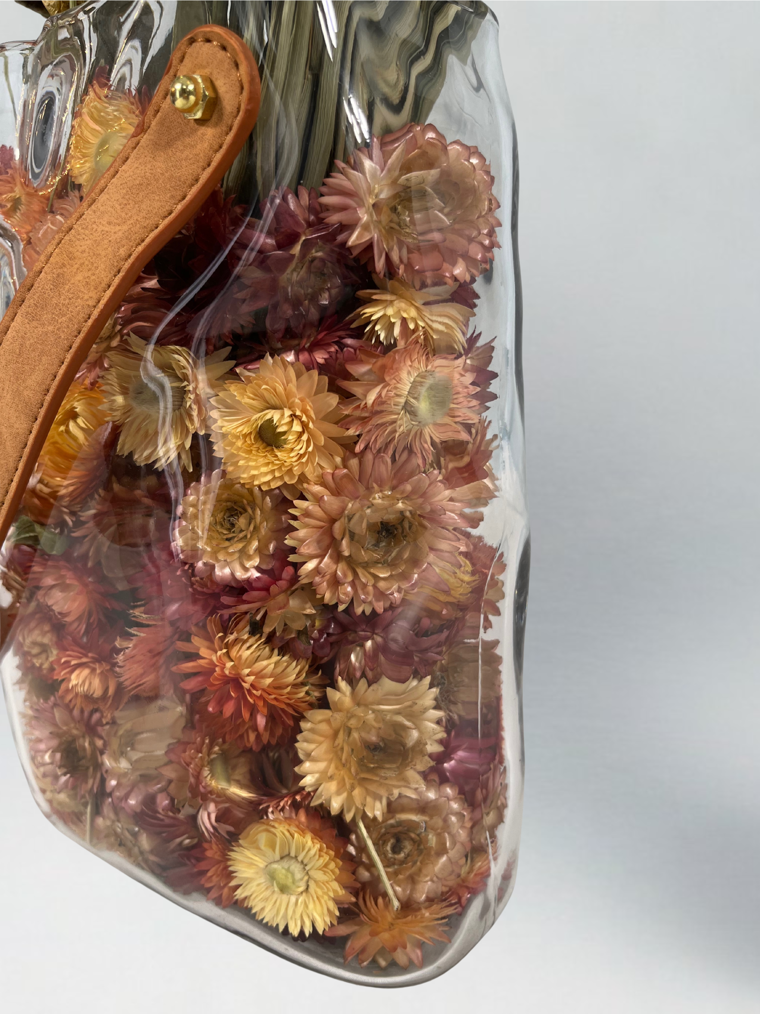 Decorative glass vase shaped like a paper bag with a leather handle filled with dried helichrysum in a natural salmon colour.