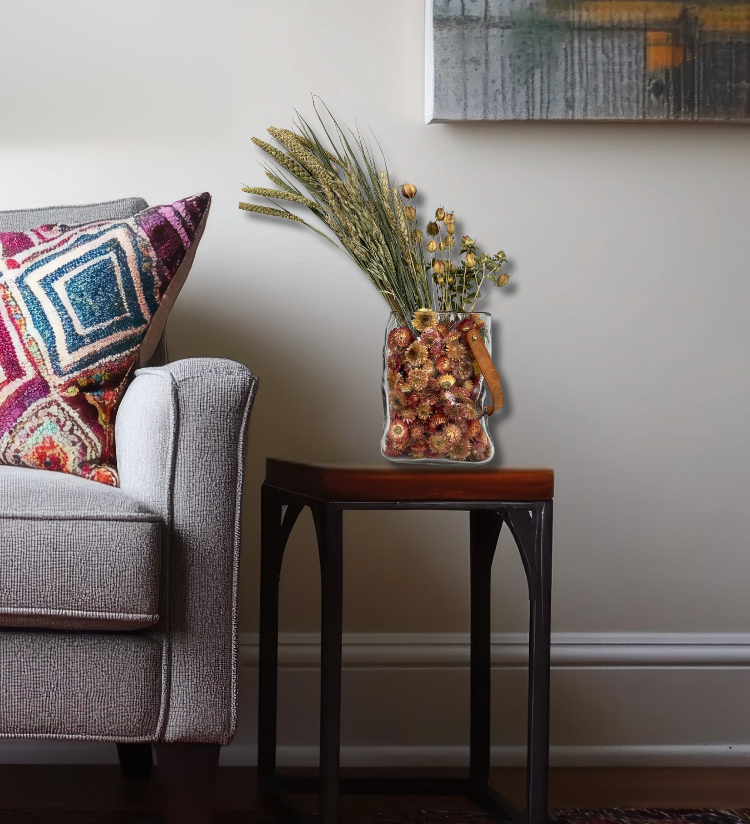 Gray sofa with colorful pillows and a small table with a beautiful dried flower arrangement in a living room setting.