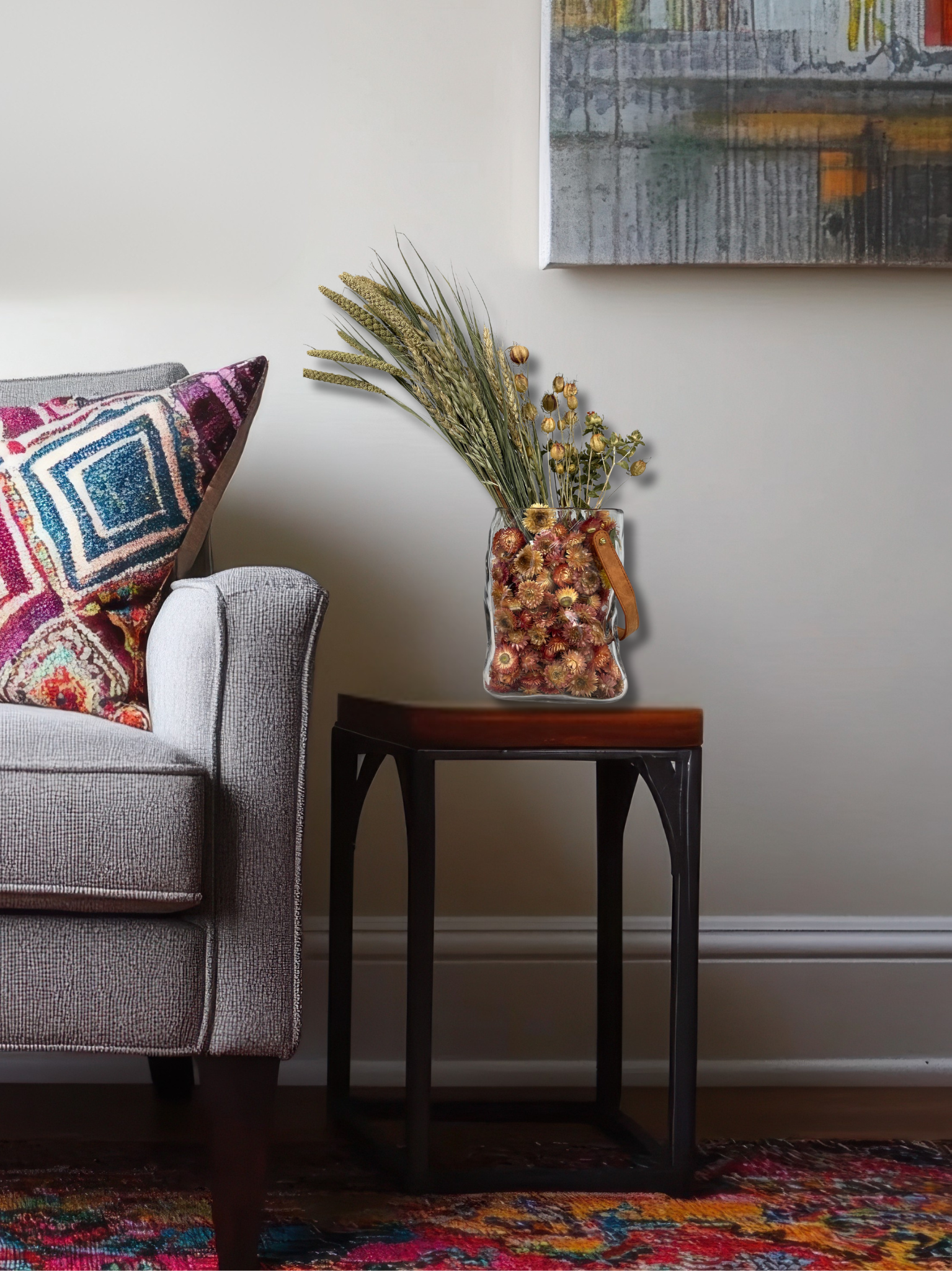 Gray sofa with colorful pillows and a small table with a beautiful dried flower arrangement in a living room setting.