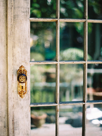 Vintage glass door with a decorative handle and keyhole, blurred green garden background