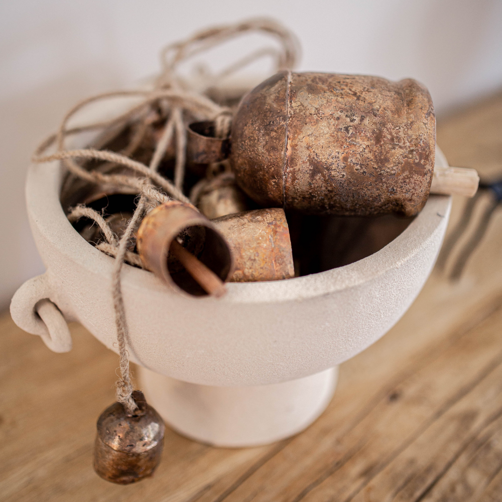 Group of brass bells in various sizes in a white ceramic bowl on a wooden surface