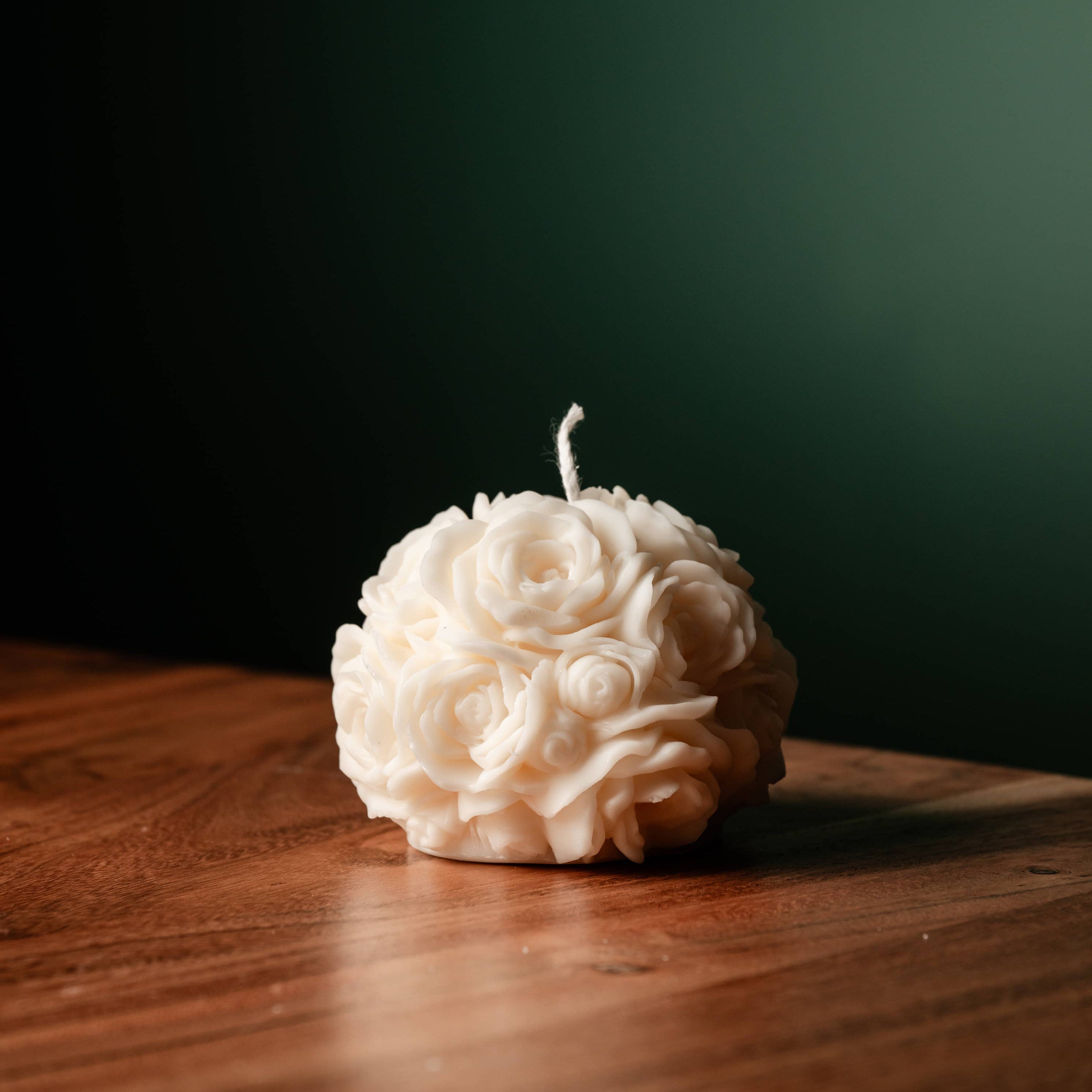 A white spherical soy wax candle embossed with a beautiful rose motif on a wooden surface.
