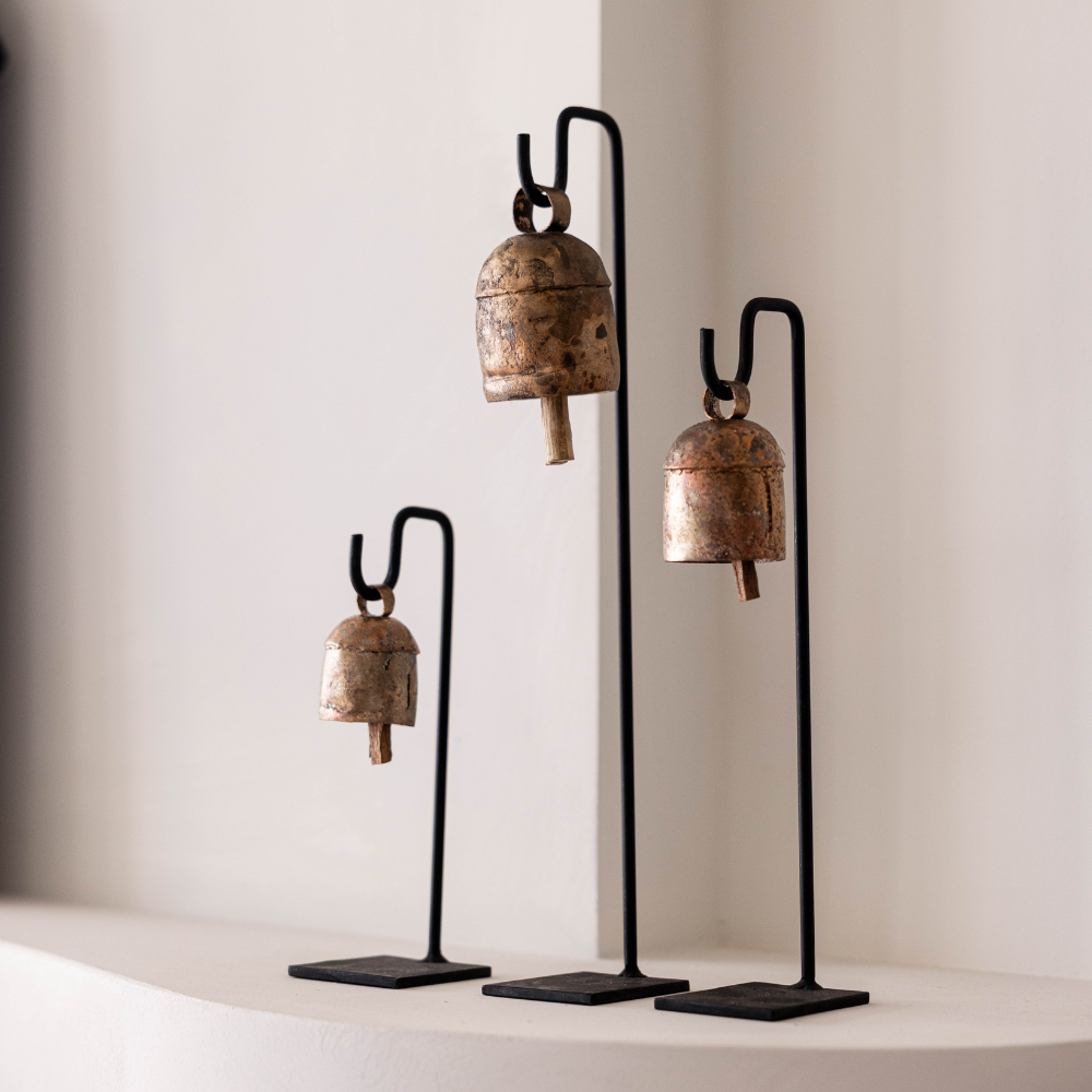 Three decorative bells on stands against a plain wall