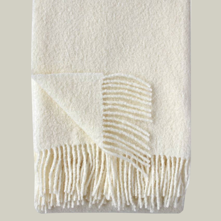 A luxurious wool blend boucle throw in ivory against a pale green background