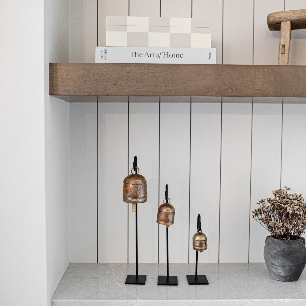 Decorative vintage bells on stands displayed on a shelf against a white panelled wall.