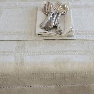 Table setting with silverware staked on a white linen napkin, with a white linen table runner and cloth