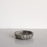 Round grey marble soap dish on a light gray surface with a white background