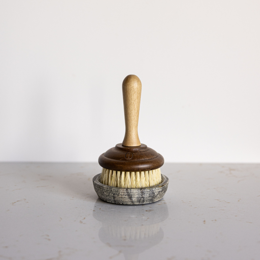 Vintage style scrub brush with wooden handle and bristle head on a grey marble dish.