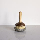 Vintage style scrub brush with wooden handle and bristle head on a grey marble dish.