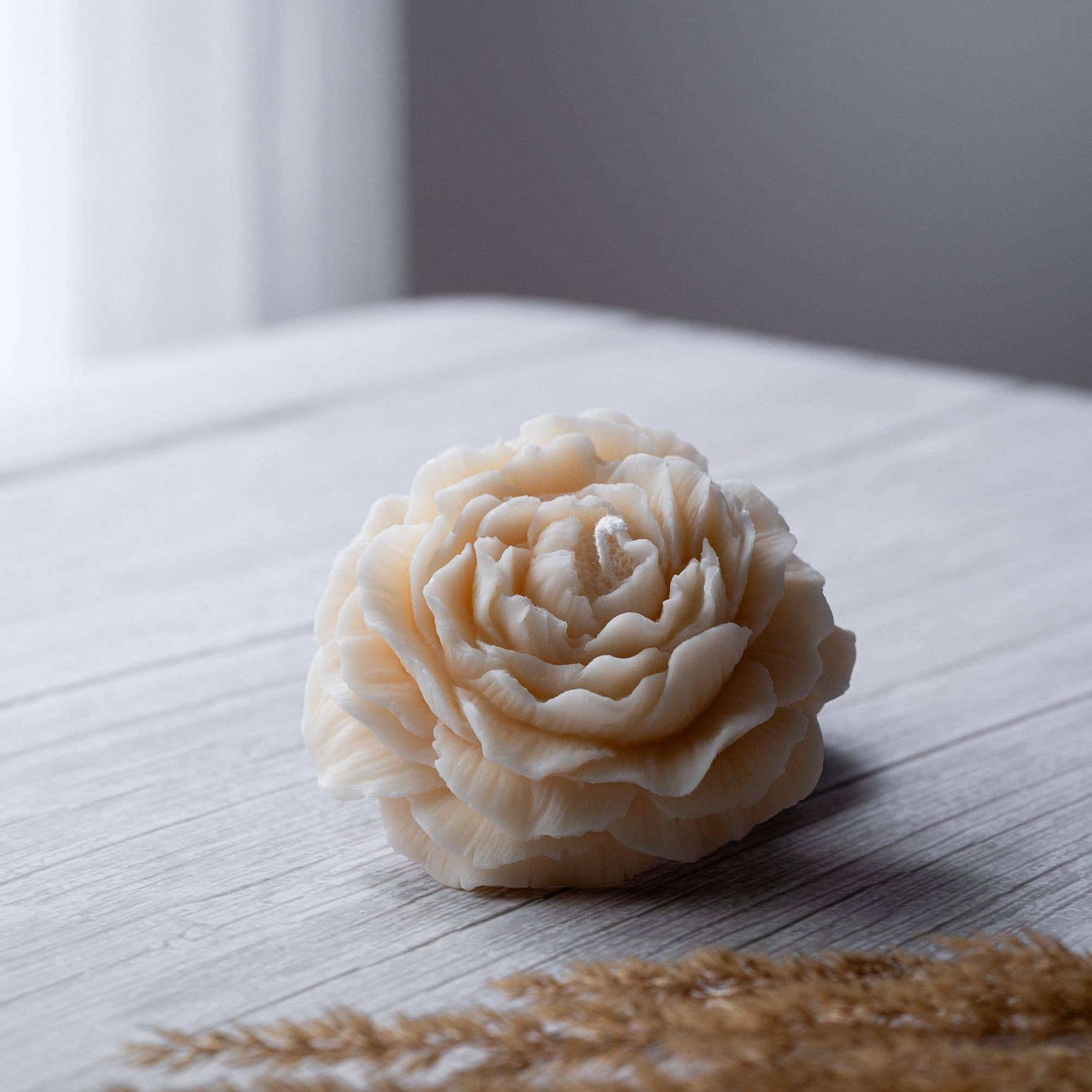 Beautiful small candle in the shape of a peony flower on a wooden surface. 