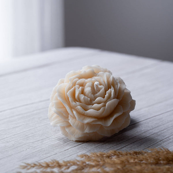 Beautiful small candle in the shape of a peony flower on a wooden surface. 