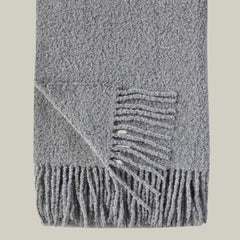 A luxurious wool blend boucle throw in grey with fringe