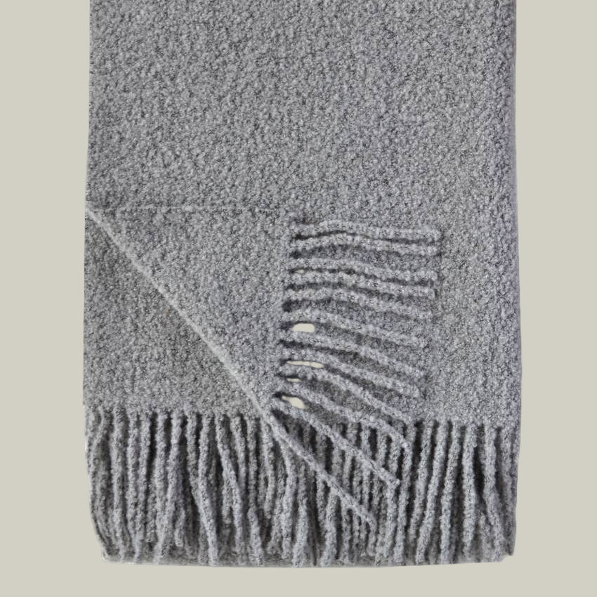 A luxurious wool blend boucle throw in grey with fringe