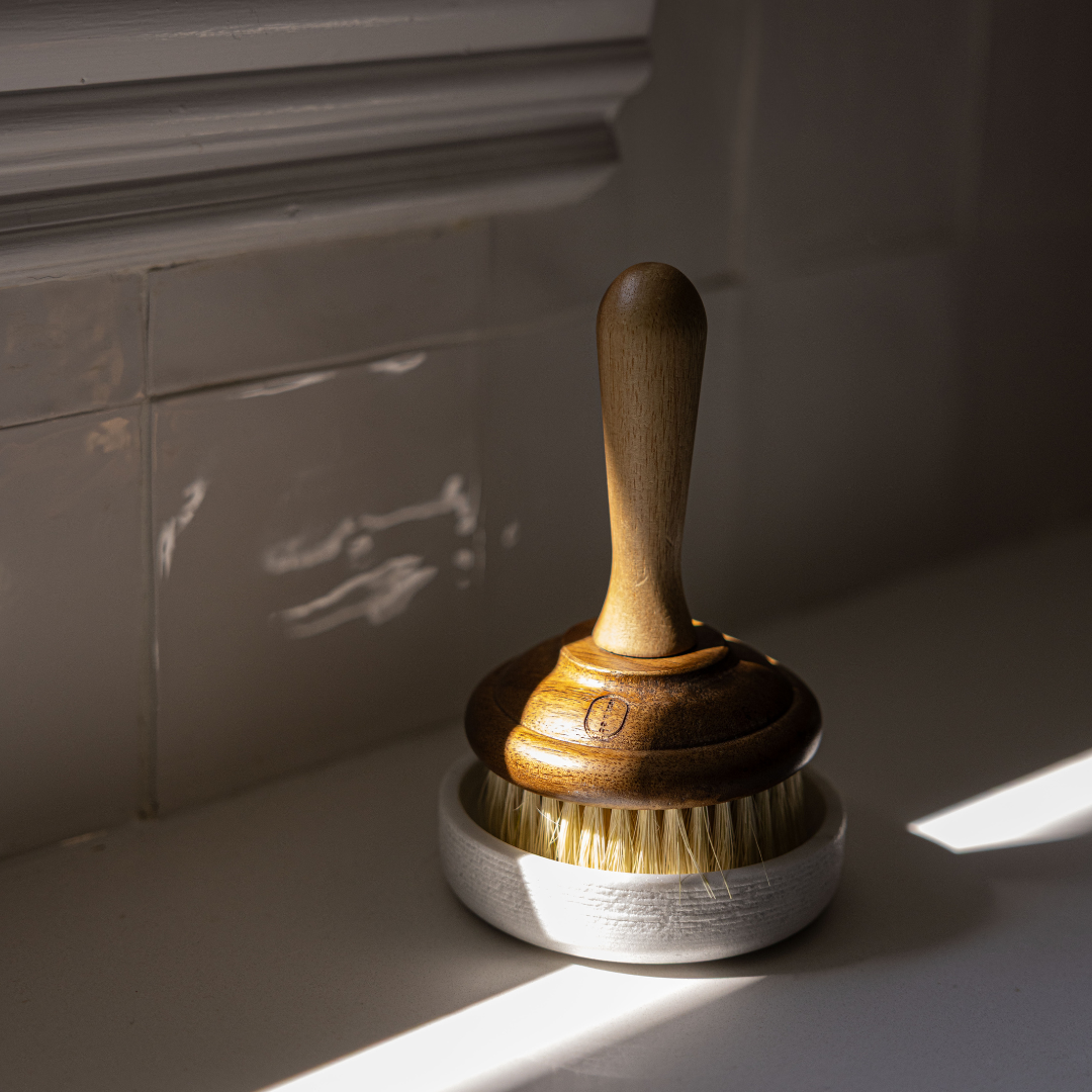 Wooden dish brush with bristles in a marble holder on a light surface.