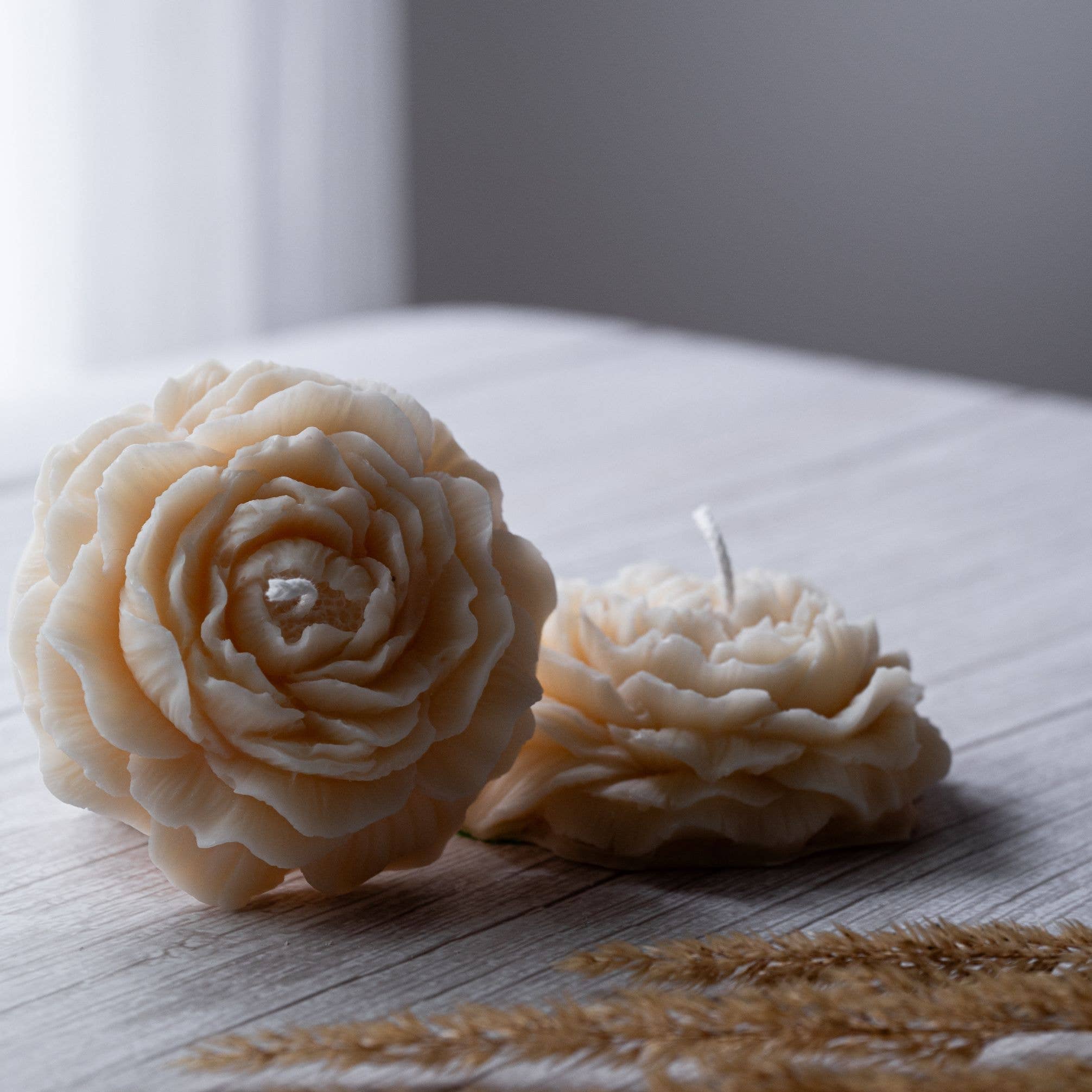 Two beautiful small candles in the shape of a peony flower on a wooden surface. 