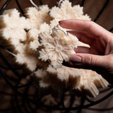 Hand holding a decorative snowflake shaped candle with a basket of similar candles in the background.