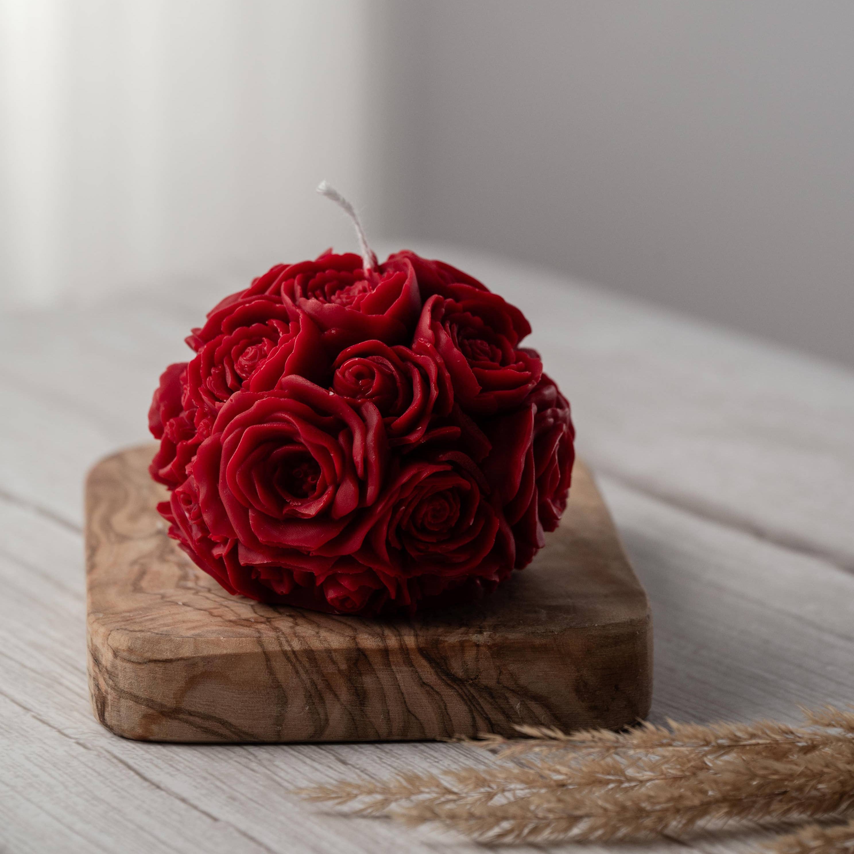 A red spherical soy wax candle embossed with a beautiful rose motif on a wooden surface.